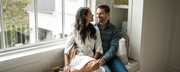 A man and woman sit together on a window seat indoors, reflecting comfort and connection, aligning with WeNatal's holistic wellness ethos.